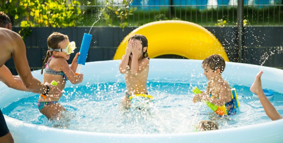 father playing with siblings and neighbors children in inflatable swimming or wading pool having fun