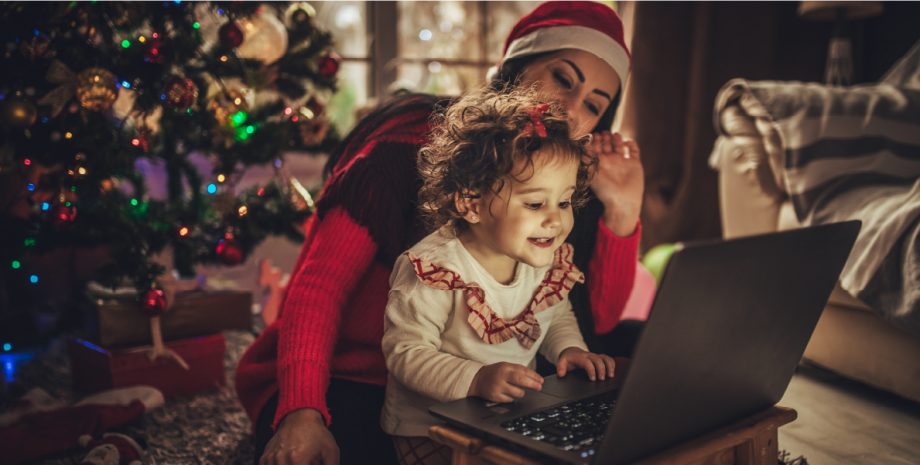 A mother and child use a computer in front of a Christmas tree.