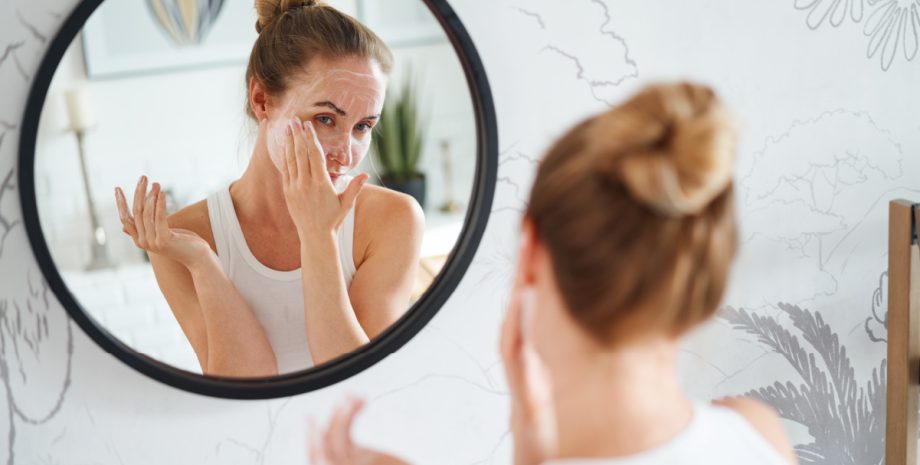 A woman applying lotion in the mirror.